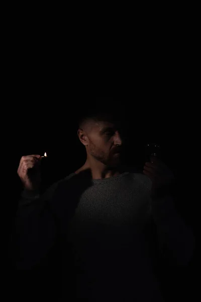 Uomo nel buio guardando lampadina elettrica, mentre tenendo partita bruciore isolato su nero — Foto stock