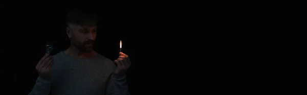 Homem durante o desligamento de energia segurando fósforo iluminado e lâmpada elétrica isolada em preto, banner — Fotografia de Stock