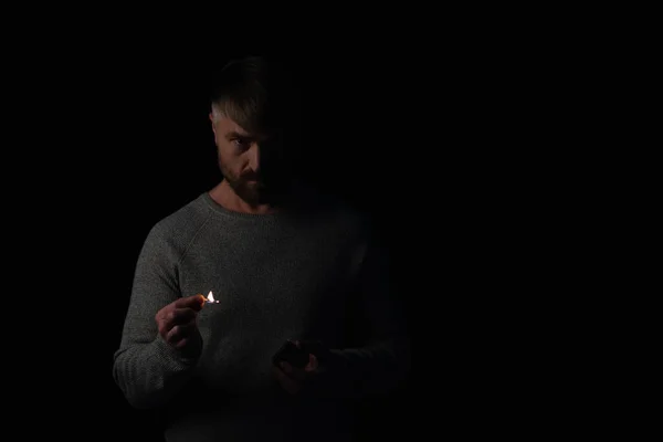 Displeased man holding burning match during energy blackout isolated on black — Stock Photo