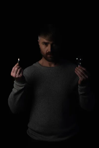 Людина з палаючим сірником і лампочкою дивиться на камеру під час відключення електроенергії ізольовано на чорному — стокове фото