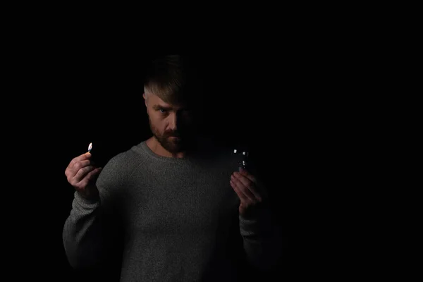 Раздраженный человек с лампочкой и горящей спичкой глядя на камеру, изолированную на черном — стоковое фото