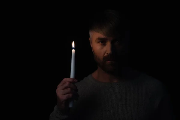 Man holding lit candle during energy blackout and looking at camera isolated on black — Stock Photo