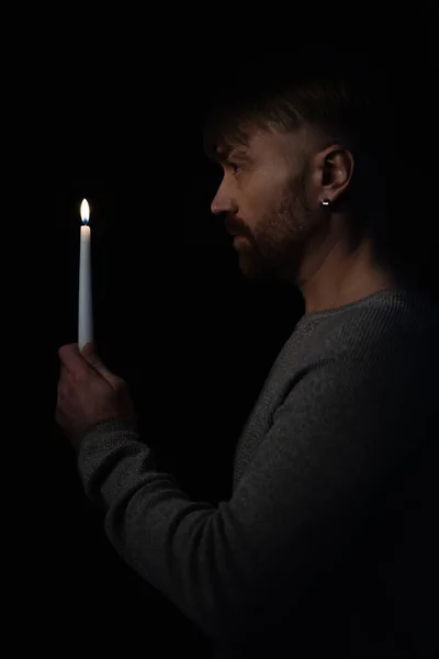 Side view of adult man holding burning candle in darkness isolated on black — Stock Photo