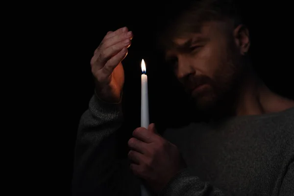 Людина в темряві, викликаний відключенням енергії, що тримає запалену свічку ізольовано на чорному — стокове фото