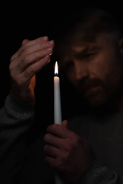Uomo mano nella mano vicino alla candela e guardando la fiamma ardente isolata sul nero — Foto stock