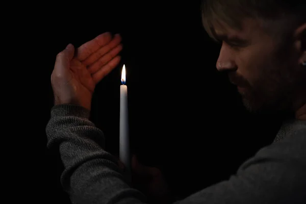 Man looking at flame of burning candle during power outage isolated on black — Stock Photo