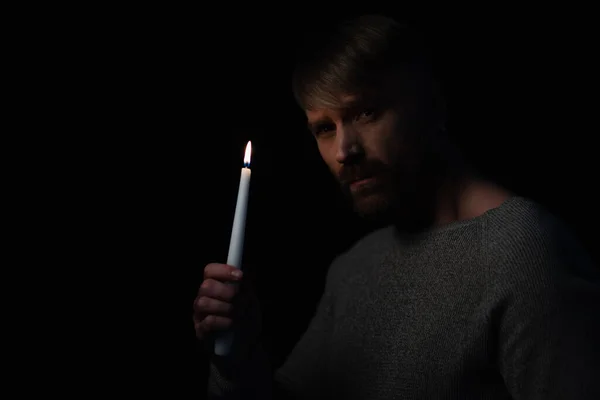 Людина з палаючою свічкою дивиться на камеру під час відключення електроенергії ізольовано на чорному — стокове фото