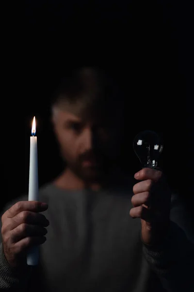 Selektiver Fokus von Glühbirne und brennender Kerze in den Händen eines verschwommenen Mannes isoliert auf schwarz — Stockfoto