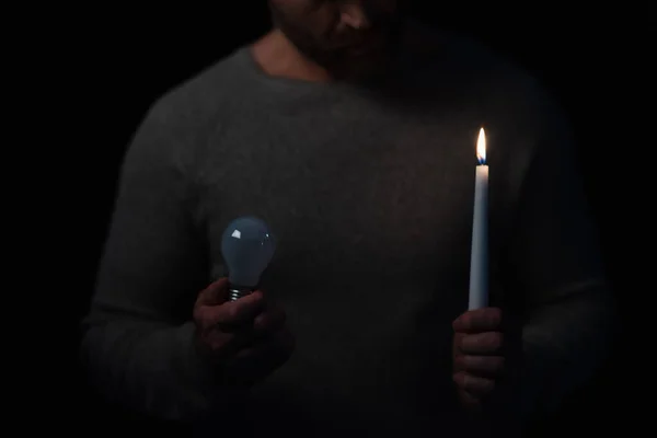 Partial view of man with burning candle and light bulb isolated on black — Stock Photo
