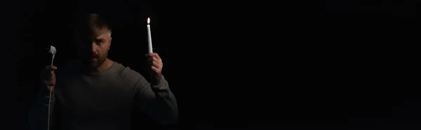 Mann mit Stecker und brennender Kerze blickt isoliert auf schwarze Kamera, Banner — Stockfoto