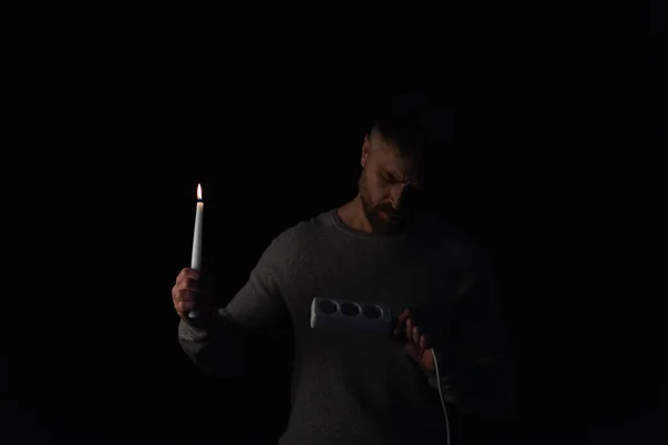 Людина з запаленою свічкою дивиться на розетку під час відключення електроенергії ізольовано на чорному — стокове фото