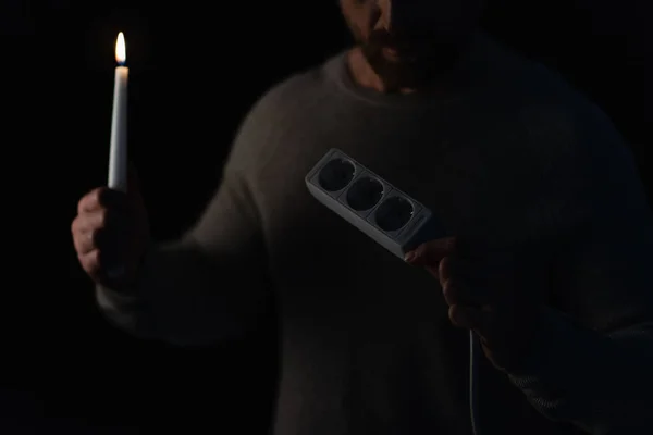 Teilbild eines Mannes mit Steckdosenverlängerung, der brennende Kerze in der Dunkelheit isoliert auf schwarz hält — Stockfoto
