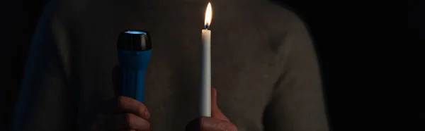 Abgeschnittene Ansicht des Mannes mit elektrischer Taschenlampe und brennender Kerze isoliert auf schwarz, Banner — Stockfoto