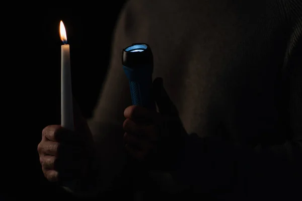 Burning candle and glowing flashlight in hands of cropped man isolated on black — Stock Photo