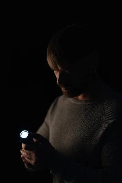 Homme tenant lampe de poche lumineux pendant une panne de courant isolé sur noir — Photo de stock