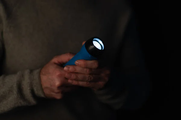 Electric flashlight glowing in darkness in hands of cropped man isolated on black — Stock Photo