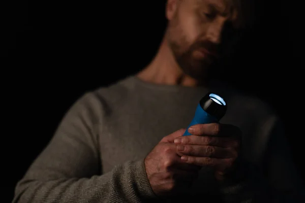 Homme flou tenant lampe de poche éclatante pendant panne d'énergie isolé sur noir — Photo de stock