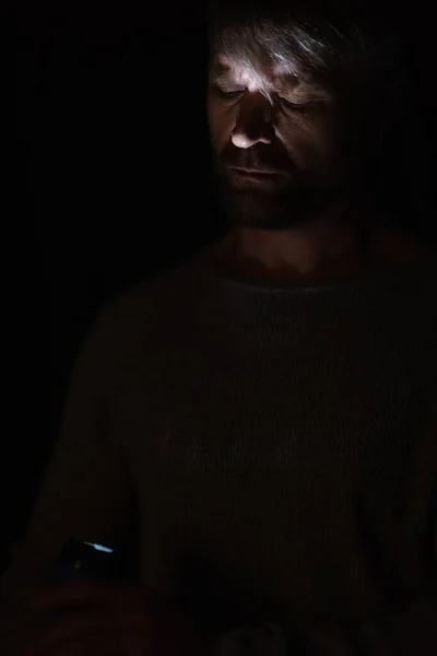 Man with glowing flashlight lighting his face during electricity blackout isolated on black — Stock Photo