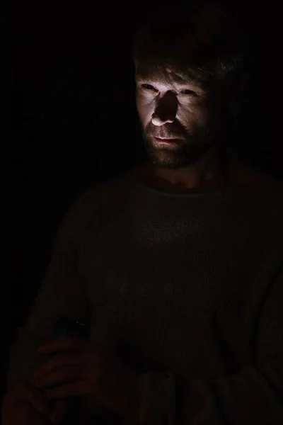 Mann beleuchtet Gesicht mit Taschenlampe, während er in der Dunkelheit isoliert auf schwarz steht — Stockfoto