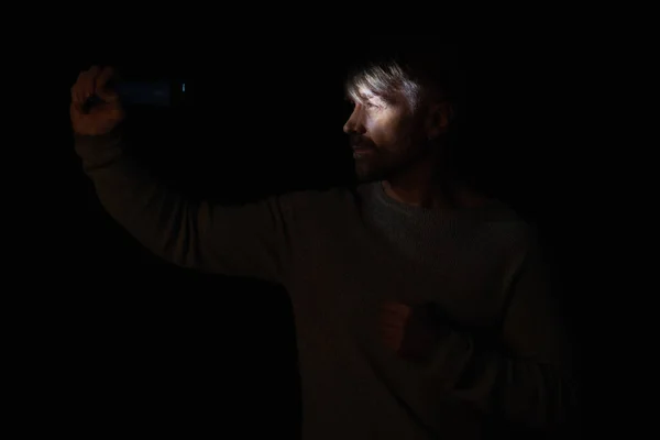 Человек с электрическим фонариком освещения его лицо во время отключения энергии изолированы на черном — стоковое фото