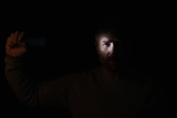 Mann im Dunkeln beleuchtet Gesicht mit Taschenlampe und sieht Kamera isoliert auf schwarz — Stockfoto