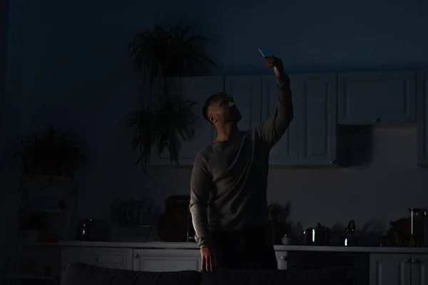 Homme tenant smartphone dans la main levée tout en cherchant une connexion pendant la panne d'énergie — Photo de stock