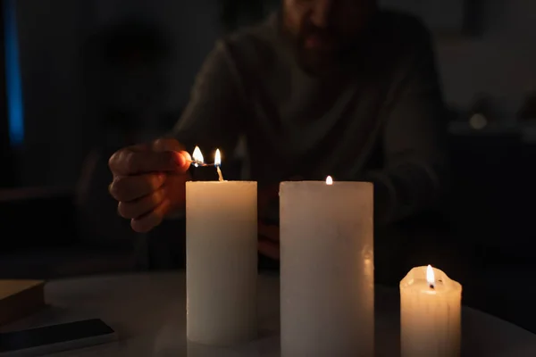 Partial view of man lighting candles near mobile phone on table during electricity outage — Stock Photo