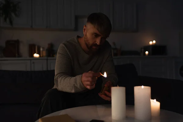 Man holding burning match while lighting candles in dark kitchen during power outage — Stock Photo