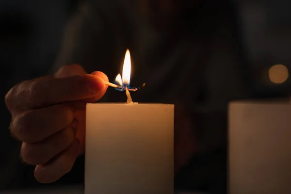 Cropped view of man with burning match lighting candle on black background — Stock Photo