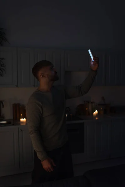 Hombre sosteniendo el teléfono celular en la mano levantada mientras capta la señal durante el corte de energía - foto de stock