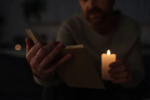 Cropped view of man holding lit candle and reading book during power outage — Stock Photo