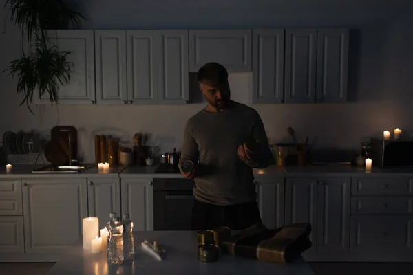 Чоловік тримає консервовану їжу біля столу з пляшковою водою та свічками — стокове фото