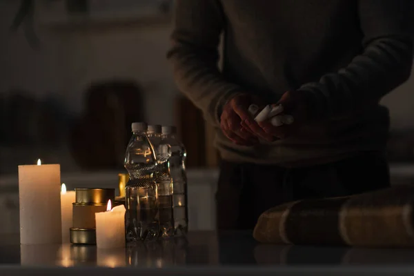 Частковий вид людини, що тримає свічки біля резерву пляшкової води та консервної їжі на столі — Stock Photo
