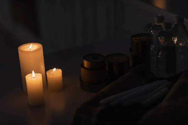 Canned food and bottled water near warm blanket and lit candles during energy outage — Stock Photo