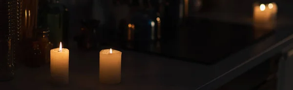 Candles burning on kitchen worktop in darkness during energy blackout, banner — Stock Photo