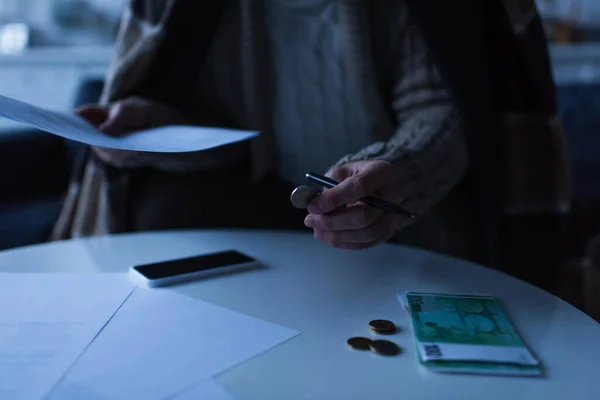 Обрезанный вид человека, держащего монеты и платежные ведомости возле банкнот евро и сотового телефона во время отключения электроэнергии — стоковое фото