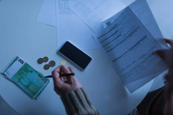 KYIV, UCRANIA - 2 DE NOVIEMBRE DE 2022: vista parcial de un hombre sosteniendo facturas cerca del dinero y el teléfono móvil en el crepúsculo - foto de stock