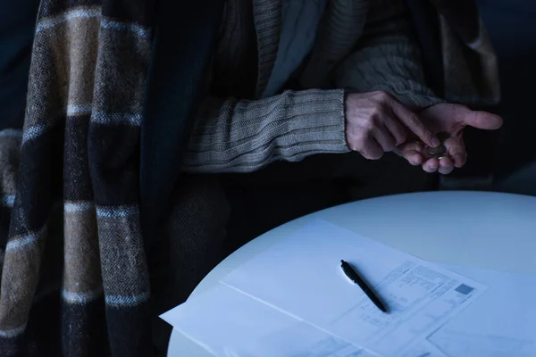 Visão parcial do homem em cobertor contando moedas perto de contas de pagamento e caneta na mesa — Fotografia de Stock