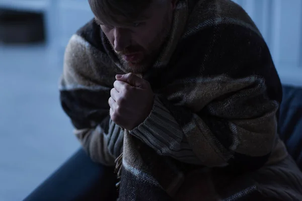 Homem congelado sentado em cobertor quente e mãos quentes durante o desligamento da eletricidade em casa — Fotografia de Stock