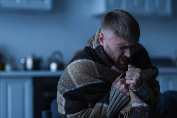 Замороженный мужчина с закрытыми глазами сидит в теплом одеяле во время отключения энергии дома — стоковое фото