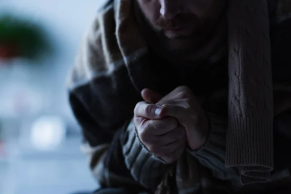 Vista recortada del hombre que calienta las manos mientras está sentado en casa bajo una manta caliente durante el corte de energía - foto de stock