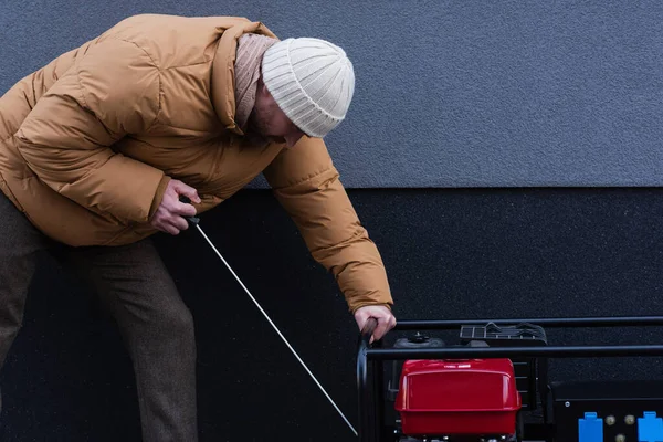 Side view of man in warm jacket and knitted hat starting power generator outdoors — Stock Photo