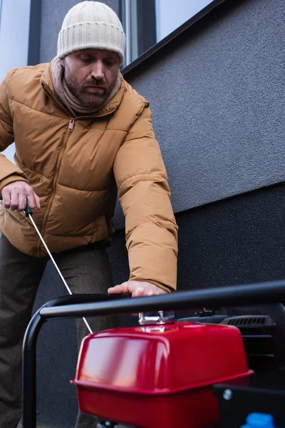 Hombre en chaqueta caliente y sombrero de arranque generador de electricidad durante el apagón de energía - foto de stock