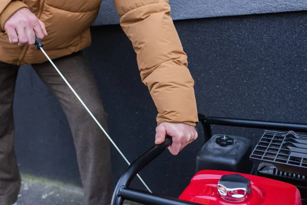 Cropped view of man in warm clothes starting power generator during electricity blackout — Stock Photo