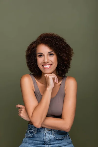 Femme afro-américaine positive en haut et jeans regardant la caméra isolée sur vert — Photo de stock
