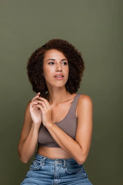 Curly african american woman in top and jeans looking away isolated on green — Stock Photo