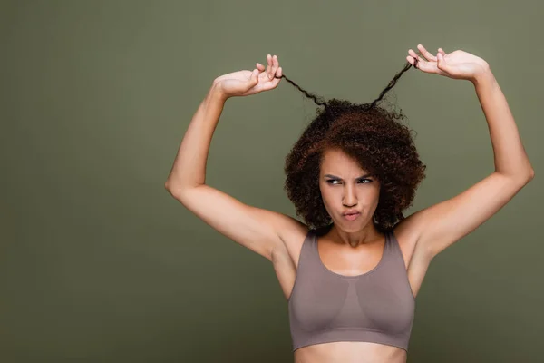 Unzufriedene afrikanisch-amerikanische Frau in Top-Berührung lockiges Haar isoliert auf grün — Stockfoto