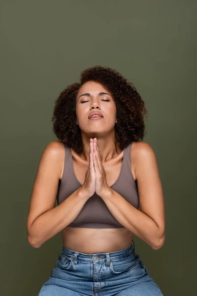 Young african american woman in top with praying hands and closed eyes isolated on green — Stock Photo
