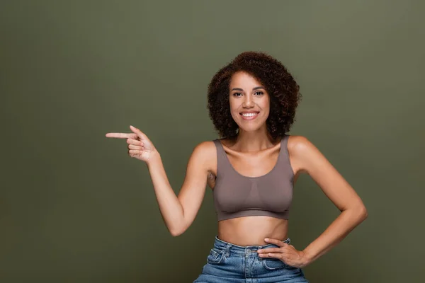 Smiling african american model in top pointing with finger isolated on green — Stock Photo