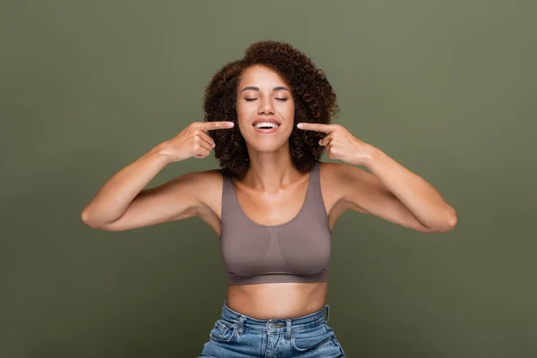 Positiva donna afro-americana in alto che punta con le dita in bocca isolate sul verde — Foto stock